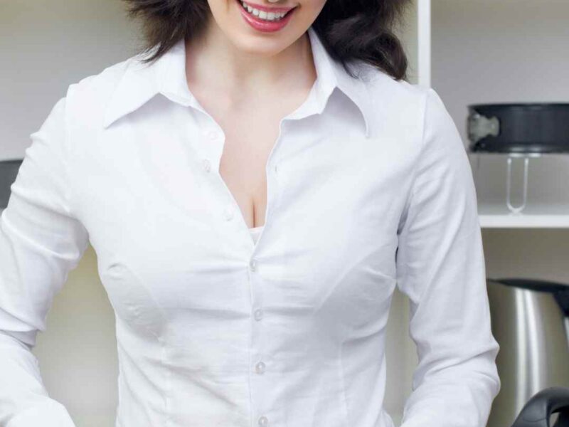 Healthy-lifestyle-habits-for-women-a- woman-in-a-white-shirt-cutting- cucumber-in-a-bright-kitchen-with-fresh-vegetables-like-carrots-green peas-and-broccoli-on the-table.