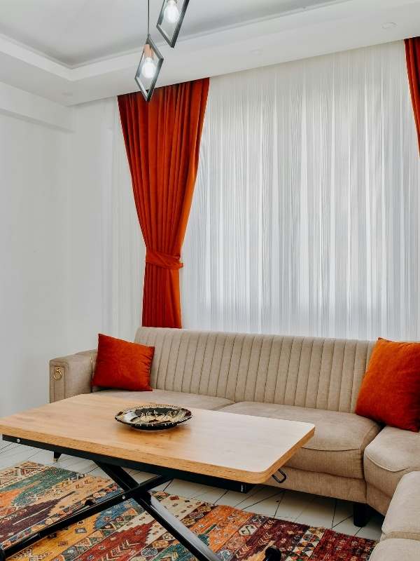 Burnt-orange-curtains-with-white-sheer-inner-drapes-coordinated-with-a-matching-area-rug-and-decorative-couch-pillows-creating-a-warm-cozy-and-colorful-living-room-aesthetic. 